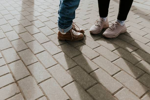 Two people wearing stylish casual shoes stand on a brick-paved street, highlighting evolving street style.